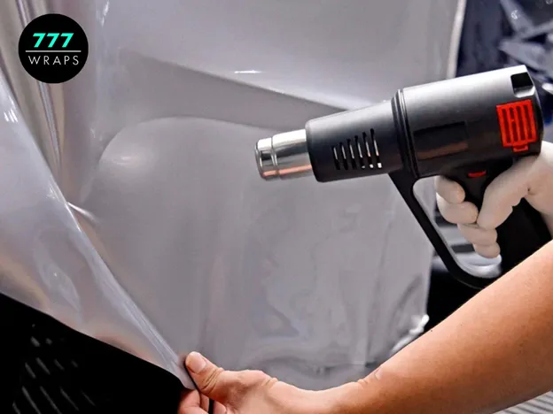 A professional installer carefully applying vinyl to a vehicle's curved surface