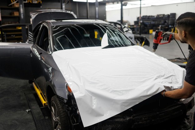 Technician applying white vinyl wrap to the front of a car.